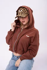 Campera cropped de color marrón con cierre frontal completo, capucha y mangas largas. Presenta un pequeño bordado blanco en el pecho y un diseño holgado.
