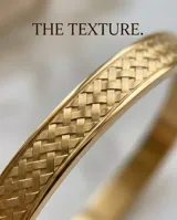 Pulsera tipo esclava rígida de acero con baño de oro, con diseño grabado de espiga en toda su superficie.