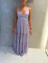 Vestido largo de color lila con tirantes finos, escote en V y diseño de falda con volados horizontales. Presenta detalles de costuras decorativas en colores contrastantes en los cortes de la falda y la cintura.