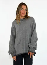 Sweater de tejido de punto en color azul marino, con cuello redondo, mangas largas con puños acanalados y ajuste holgado. Presenta un pequeño aplique decorativo en el ruedo.