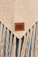 Poncho triangular tejido artesanalmente en telar manual, de lana merino color beige, con cuello alto y flecos largos en los bordes.