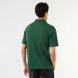 Remera polo de piqué de algodón color verde oscuro, de manga corta, con cuello camisero y cartera de tres botones. Presenta una textura sutil de líneas horizontales en relieve y una pequeña etiqueta decorativa en el borde inferior.