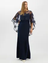 Vestido largo de corte sirena en color azul marino, confeccionado en tejido de punto con caída fluida. Presenta una capa integrada de tul fino sobre los hombros y espalda, decorada con bordados florales a tono y lentejuelas brillantes. Posee escote redondo y cierre invisible en la espalda.