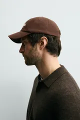 Gorra de seis paneles confeccionada en tejido de algodón, color marrón, con bordado frontal en color crema que incluye texto. Cuenta con ajuste en la parte posterior.