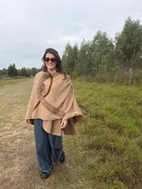 Capa de lana color beige con detalles de apliques en cuero y tejido trenzado decorativo en el frente.