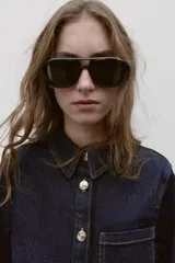 Camisa entallada de denim azul oscuro con cuello solapa, manga larga y cierre frontal con botones metálicos. Presenta un bolsillo de plastrón en el pecho y costuras a contratono.