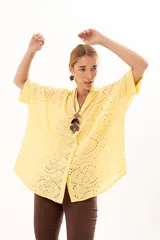 Camisa de corte oversize confeccionada en tela bordada con diseño calado, color amarillo. Presenta cuello mao, cierre frontal con botones y mangas cortas amplias.