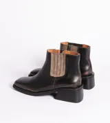 Bota corta tipo chelsea de cuero vacuno color negro, con puntera cuadrada, taco cuadrado de madera y detalle de textura grabada en el panel elástico lateral.