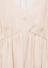 Vestido largo de corte evasé en color beige, confeccionado en tejido fluido con textura. Presenta escote en pico, tirantes finos y delicados detalles de abalorios bordados en toda la prenda.