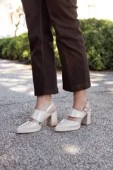 Zapato de cuero color beige, con punta fina, tira sobre el empeine y pulsera con hebilla al tobillo. Tiene talón descubierto y taco cuadrado.
