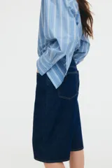 Bermuda de denim azul oscuro, tiro alto, corte ancho, largo a la rodilla y cinco bolsillos. Cierre frontal con botón.