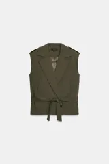 Chaleco de cuello solapa y escote pico cruzado, con hombreras y manga sisa. Presenta bolsillos de vivo en el delantero, forro interior y cierre frontal cruzado con botones. Incluye un cinturón de lazada en el mismo tejido.