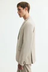Blazer slim fit de botonadura sencilla en color beige, con solapas de muesca, bolsillos con solapa y cierre de botones.
