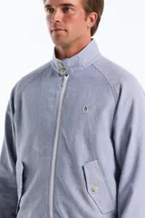 Campera estilo Harrington de corte clásico con diseño de rayas finas verticales en tono celeste y blanco. Cuenta con cuello alto, cierre frontal completo, bolsillos diagonales con solapa y botones, además de puños y dobladillo elastizados. Presenta el logo bordado del pingüino característico en el pecho.