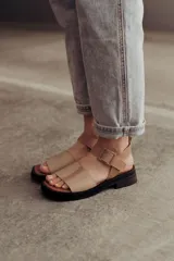 Sandalia de cuero color tostado con tiras anchas, tira en el talón y hebilla metálica rectangular ajustable. Cuenta con suela de goma con tacón bajo y plataforma.
