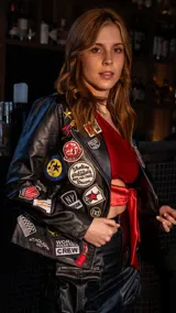 Chaqueta negra de cuero sintético con cierre frontal y múltiples parches bordados.