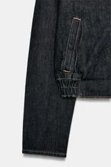 Cazadora bomber de denim color azul oscuro, con escote en pico, cierre frontal cruzado con botones a presión y bajo elástico en los laterales. Cuenta con mangas largas y bolsillos de vivo.