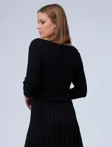 Vestido negro tejido de largo midi, con escote asimétrico adornado con tachas doradas, corte a la cintura y falda plisada. Marca Emma & Michele.