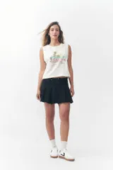 Musculosa Roxy color crudo, con cuello redondo y diseño sin mangas con sisas amplias. Presenta un estampado frontal con la palabra 'Roxy' en tonos degradados de rosado y celeste, acompañado de palmeras, un sol y la leyenda 'Sunsets Chaser'.