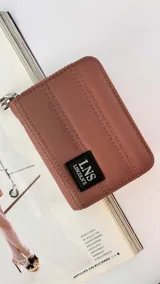 Billetera corta de diseño acolchado con cierre perimetral, confeccionada en material sintético color rosado. Presenta costuras verticales decorativas y un parche frontal con el logo de la marca LNS.