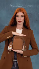 Bandolera porta celular color lila, confeccionada en material sintético con textura granulada. Cuenta con cierre frontal, compartimento principal con cierre y correa larga regulable con diseño geométrico en tonos pasteles.