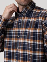Camisa de manga larga de franela de algodón orgánico con estampado a cuadros en tonos azul marino, mostaza, blanco y marrón. Presenta cuello clásico, cierre frontal con botones de madera y dos bolsillos en el pecho.