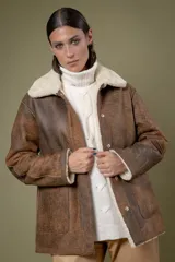 Campera tipo borrego de cuero con efecto desgastado, con interior y cuello de piel sintética en color crema. Presenta cierre frontal con botones a presión y bolsillos frontales amplios.
