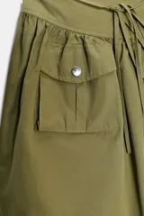 Falda corta de tiro medio en color verde militar. Presenta un diseño con volumen, pliegues, un bolsillo de plastrón en el delantero y detalle de trabilla con hebilla metálica en la cintura. Incluye cierre lateral con cremallera oculta.