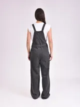 Monoprenda larga de denim gris oscuro, con diseño estilo overall, tirantes ajustables, cierre frontal de botones metálicos y bolsillos frontales grandes. Incluye un cinturón ajustable del mismo material.