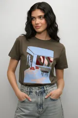Remera de algodón color verde militar con cuello redondo y estampa frontal artística que representa una escena de interior.