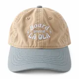 Gorro con visera color beige y visera celeste, con bordado frontal en hilo blanco que dice "Board brand LA OLA" junto con pequeños símbolos de rayos.