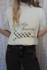 Remera de algodón color beige con estampa frontal que incluye la frase 'Jardín de Invierno' y un diseño gráfico de un animal con patrón de cuadros.