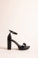 Sandalias de tacón alto con plataforma, confeccionadas en cuero con acabado brillante tipo charol, color negro. Poseen tira delantera ancha, tira ajustable al tobillo con hebilla metálica dorada, y taco ancho.