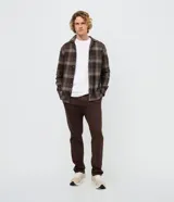 Pantalón slim de sarga lavada color marrón, con cierre de botón y cremallera, trabillas para cinturón y bolsillos laterales y traseros.