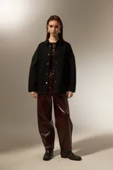 Sobrecamisa de jean color negro, con cierre frontal de botones metálicos, mangas largas y detalle de pequeñas tachas decorativas en la parte superior delantera.