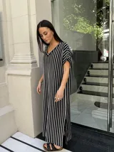 Vestido largo de tejido de punto con diseño de rayas verticales en blanco y negro. Presenta escote en V, mangas cortas y tajos laterales en el ruedo para mayor movimiento.