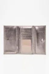 Billetera tipo sobre color champagne, con textura de cuero granulado y cierre de solapa. Presenta una placa metálica rectangular con el nombre de la marca grabado en el frente.