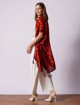 Kimono ligero de poliéster con estampado geométrico en tonos rojo oscuro y naranja. Presenta mangas anchas y terminación con borlas en los ruedos.