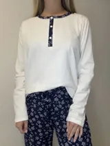 Pijama de algodón compuesto por una remera blanca de manga larga con cuello redondo, botones frontales y ribete con detalle estampado, acompañado de un pantalón azul marino con estampado floral y cordón ajustable en la cintura.