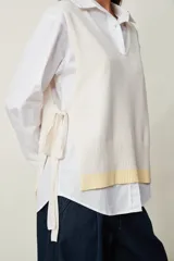 Chaleco de punto color beige claro con escote en V, sin mangas y diseño abierto en los laterales con ajuste de cintas para atar.