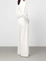 Pantalón blanco de pierna ancha y recta, estilo pareo, con cruce frontal envolvente y cintura elástica en la espalda. Presenta bolsillos laterales y falsos bolsillos traseros.