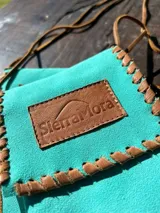 Funda para celular de gamuza azul marino con correa de cuero marrón y aplique de cuero marrón con logo de la marca.