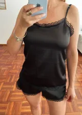 Conjunto de pijama negro de satén, compuesto por un top de breteles finos con escote recto y detalle de encaje en el borde, y un short con cintura elástica y detalle de encaje en el ruedo.