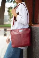 Bandolera de diseño clásico en color bordó, confeccionada en material simil cuero. Cuenta con bolsillos frontales de acceso rápido, compartimento principal con cierre metálico y portallaves interior. Incluye dos correas intercambiables para mayor versatilidad.