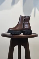 Bota de caña corta color marrón, con cierre lateral y suela track negra de goma con plataforma.