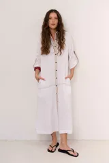 Vestido chemise midi blanco de manga larga con cierre frontal de botones, bolsillos laterales y costuras a la vista en contraste.