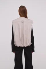 Chaleco color caqui con cierre frontal con cremallera, bolsillos con solapa y corte holgado.