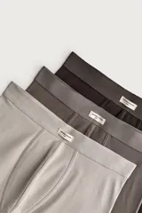 Pack de tres calzoncillos tipo bóxer de algodón elástico, en tonos gris claro, gris topo y marrón oscuro, con cintura elástica y pequeña etiqueta frontal con inscripción.
