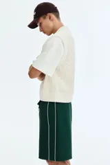 Short de corte relajado de color verde oscuro, con cintura elástica y cordón ajustable. Cuenta con ribetes de cinta blanca a lo largo de los laterales y bolsillos frontales.