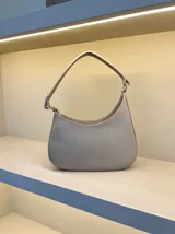 Cartera tipo hobo de cuero con textura granulada, diseño de media luna y asa fija para llevar al hombro.